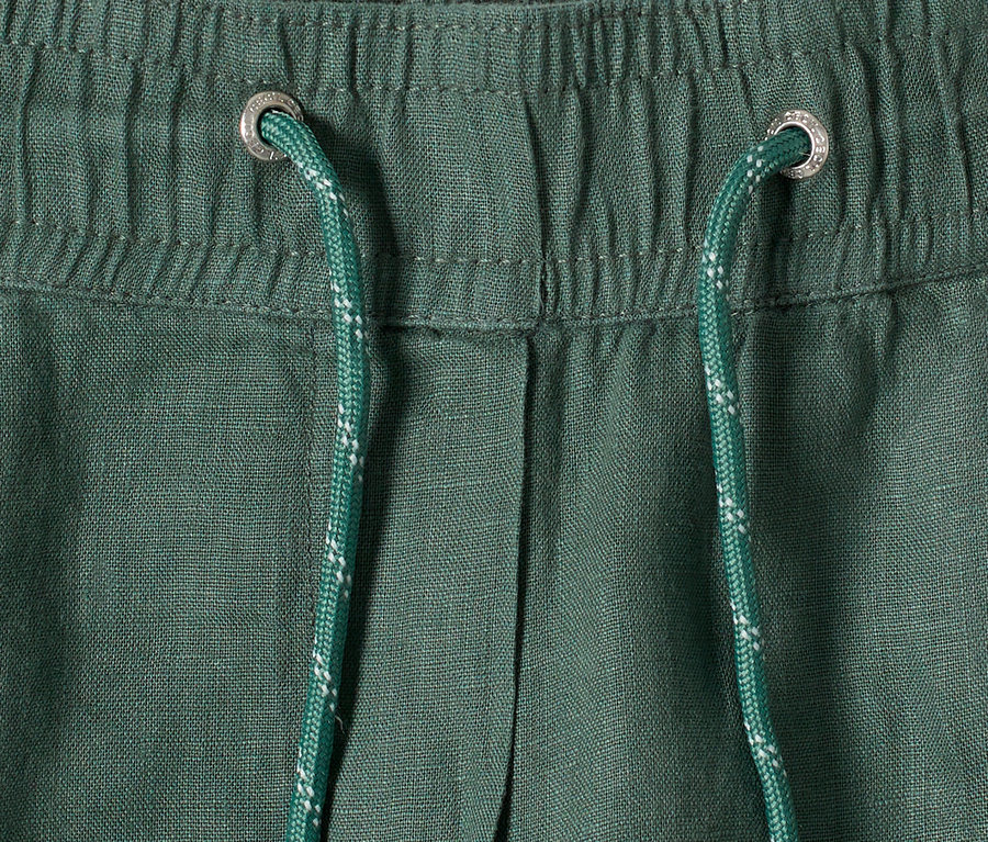 Nahaufnahme einer grünen Hose mit Tunnelzug und silbernen Ösen.