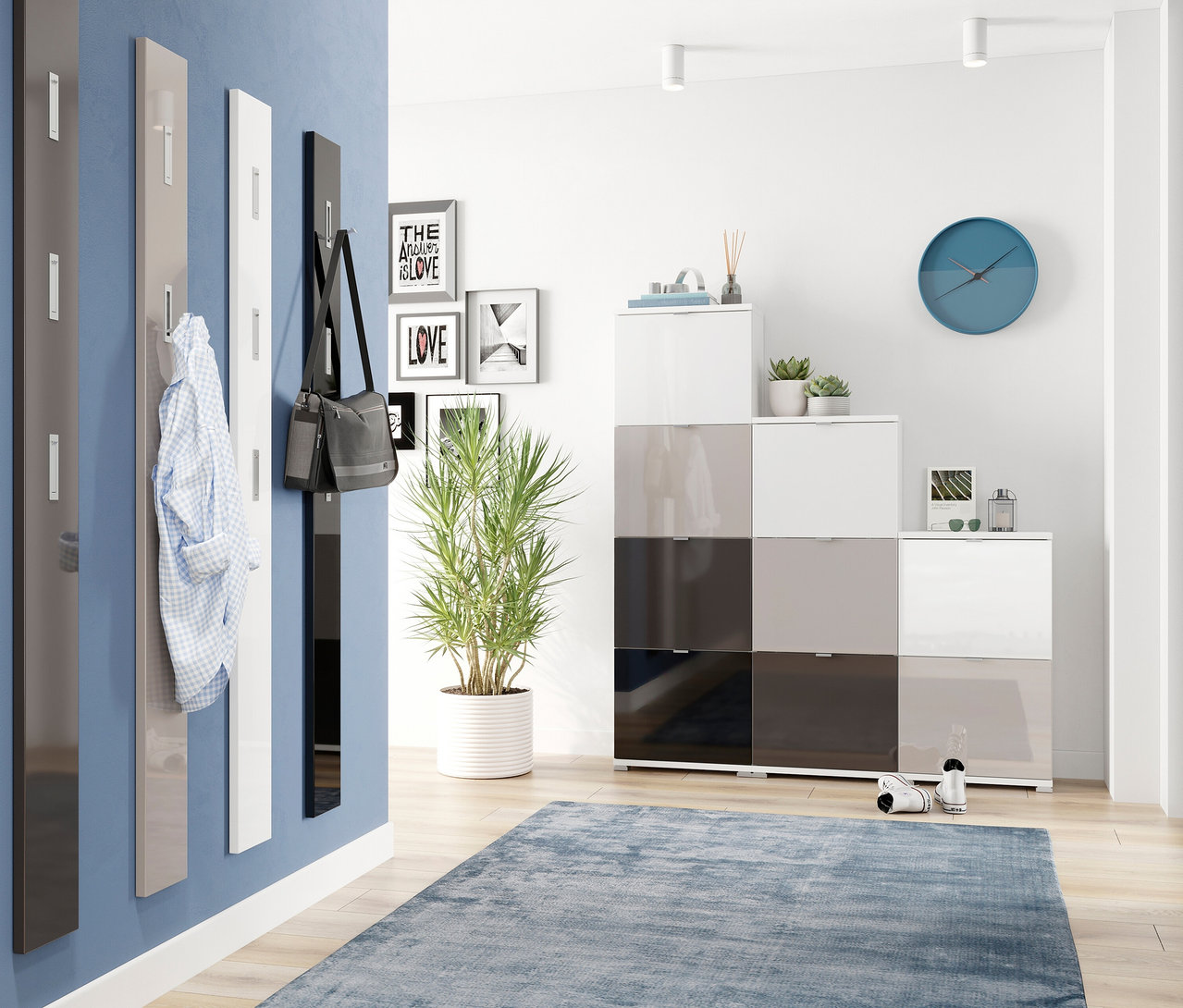 Ein Flur mit blauer Wand, an der vier Garderobenpaneele mit silberfarbenen Haken hängen: ein graphitfarbenes, ein kaschmirfarbenes mit einem Hemd, ein weißes und ein schwarzes mit einer Tasche. Rechts steht ein modularer Schuhschrank in Weiß, Kaschmir und Graphit, davor ein blauer Teppich.