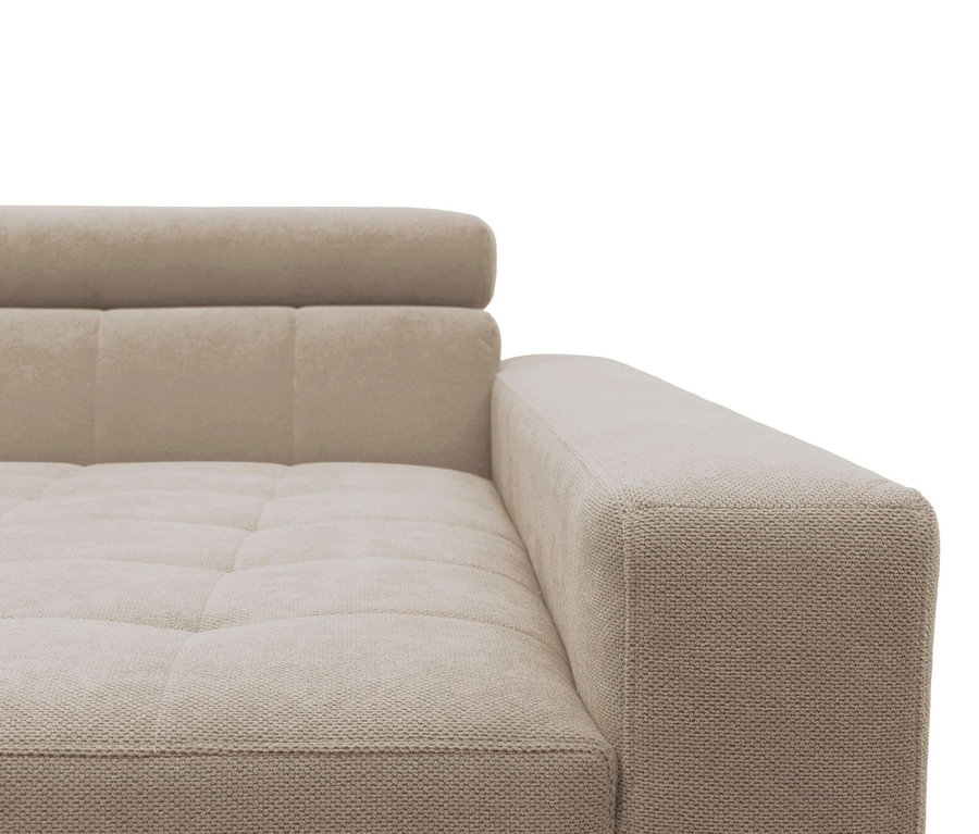 Nahaufnahme eines beigefarbenen Sofas mit strukturiertem Stoff, einer getufteten Sitzfläche und Rückenlehne sowie einer quadratischen Armlehne rechts.