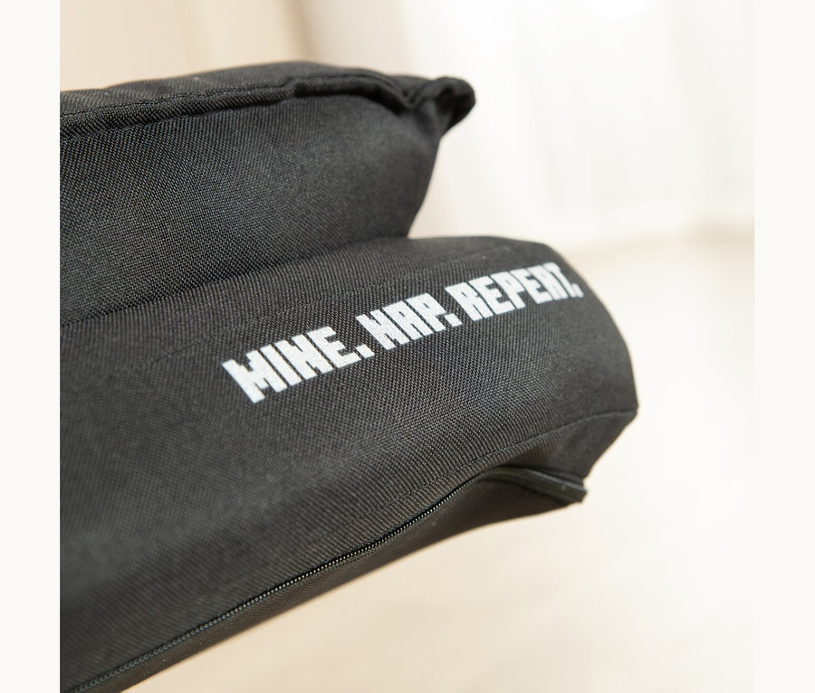 Nahaufnahme eines schwarzen Stoffartikels mit weißem Text „MINE. NAP. REPEAT.“ und einem sichtbaren Reißverschluss.