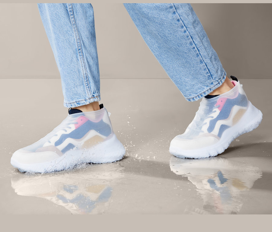 Beine in Jeans gehen in Regen-Überziehschuhen durch eine Pfütze.