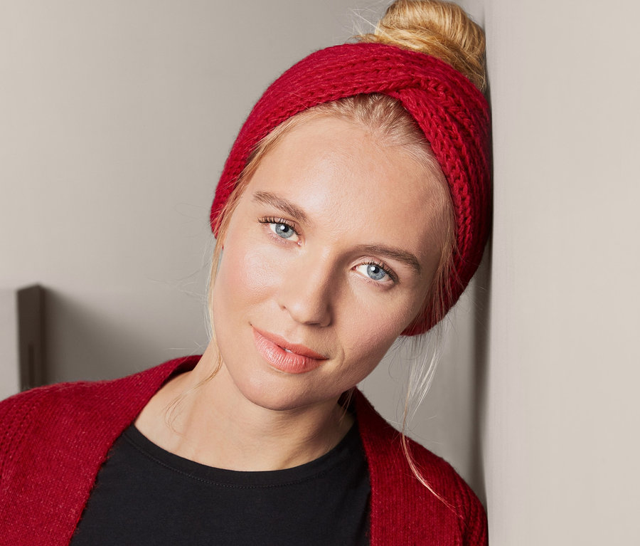 Blonde Frau lehnt an der Wand und trägt ein rotes Strickstirnband.