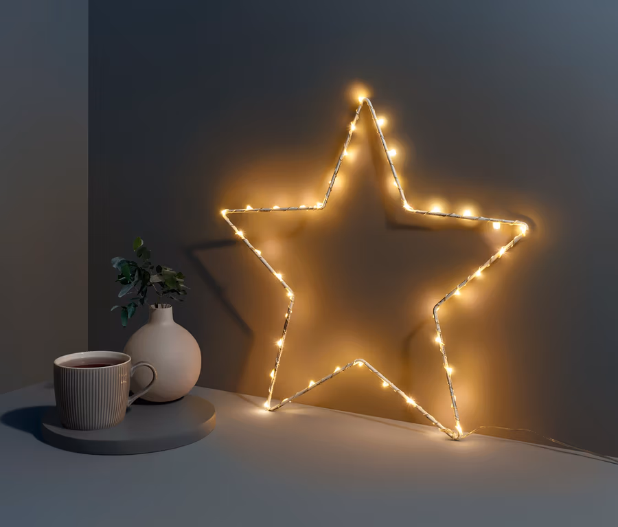Kleiner LED-Metallstern steht neben Tasse und Vase auf einem Tisch.