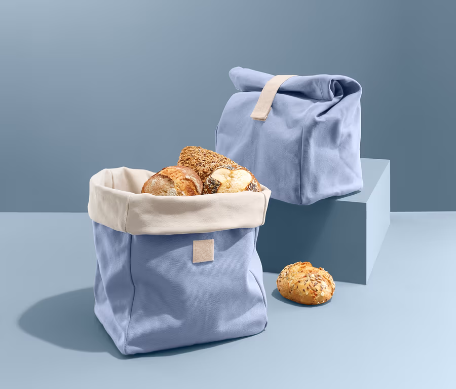 Ein offener blauer 2-in-1-Brotbeutel gefüllt mit Brotlaiben neben einem geschlossenen Brotbeutel.