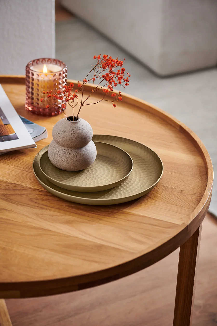 Auf einem Holztisch liegen zwei Dekotabletts, eine Vase mit Blumen und eine Kerze.