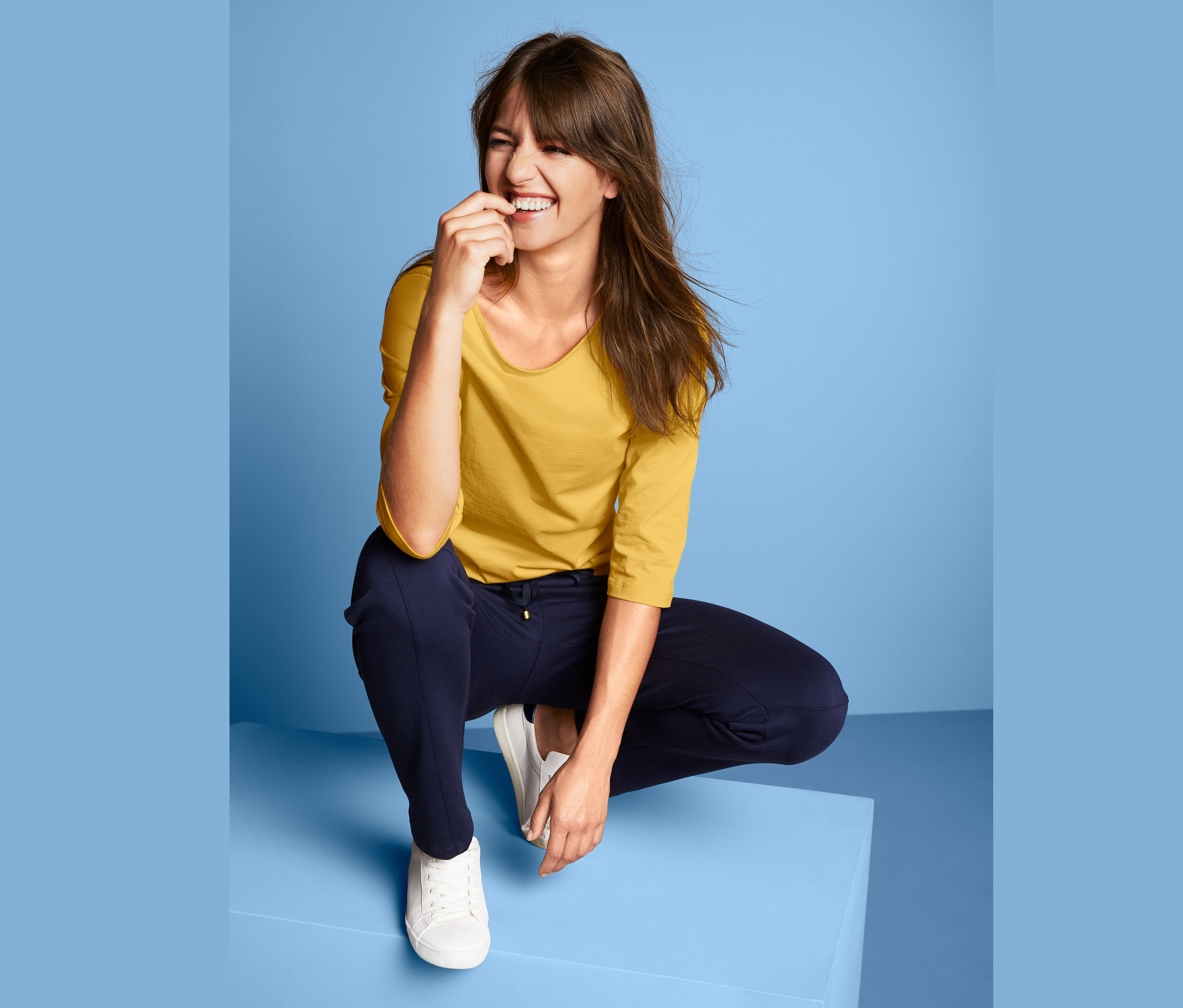 Frau hockt in gelbem Shirt mit U-Boot-Ausschnitt.