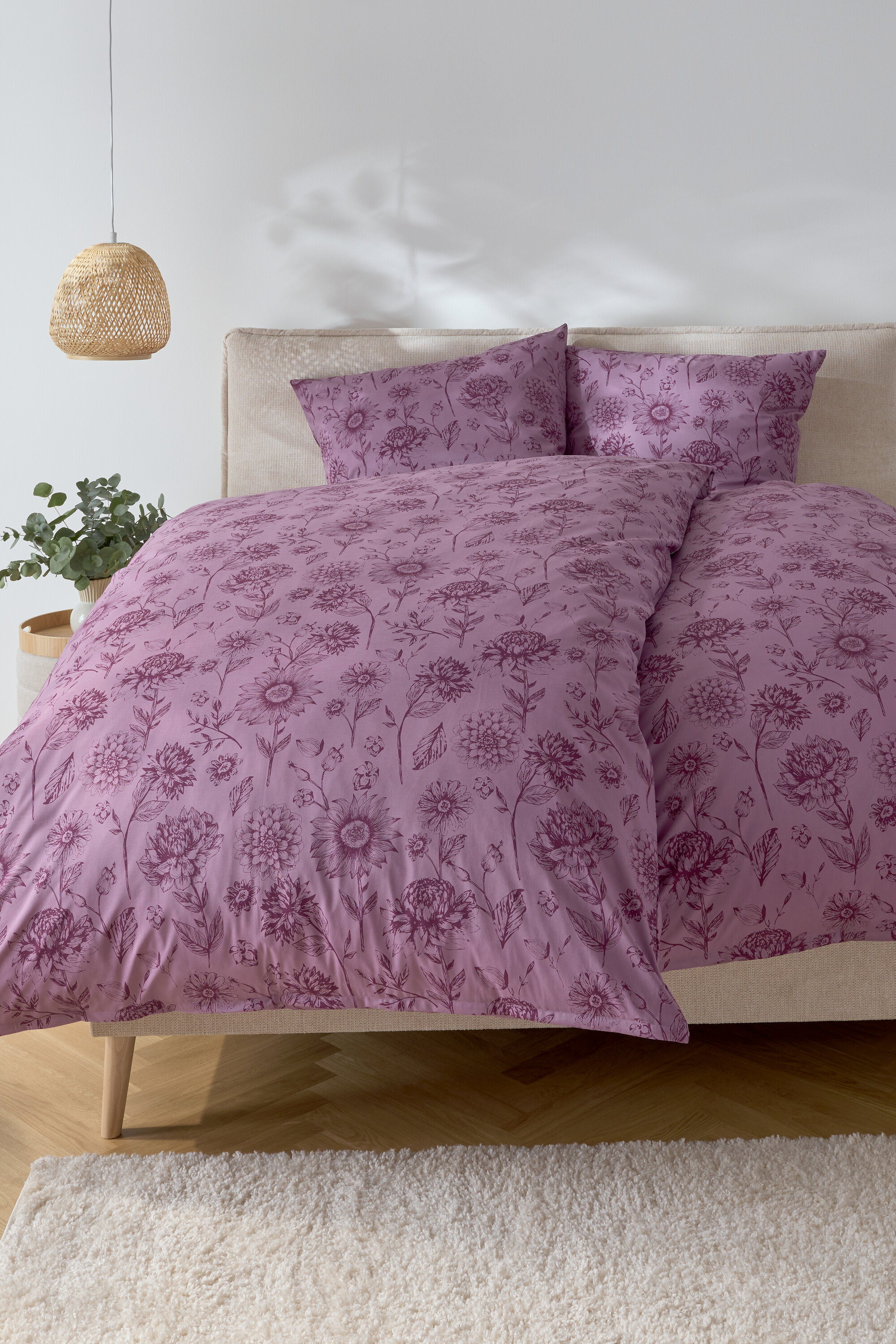 Schlafzimmer mit einem Bett mit lila Blumendruck-Bettwäsche und zwei Kissen.