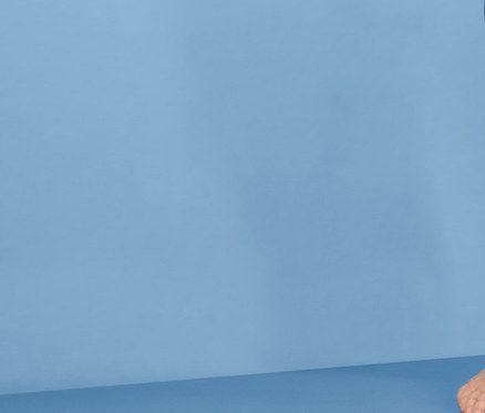 Lächelnde Frau posiert in grauem Tanktop und Jersey-Relaxhose vor blauem Hintergrund.