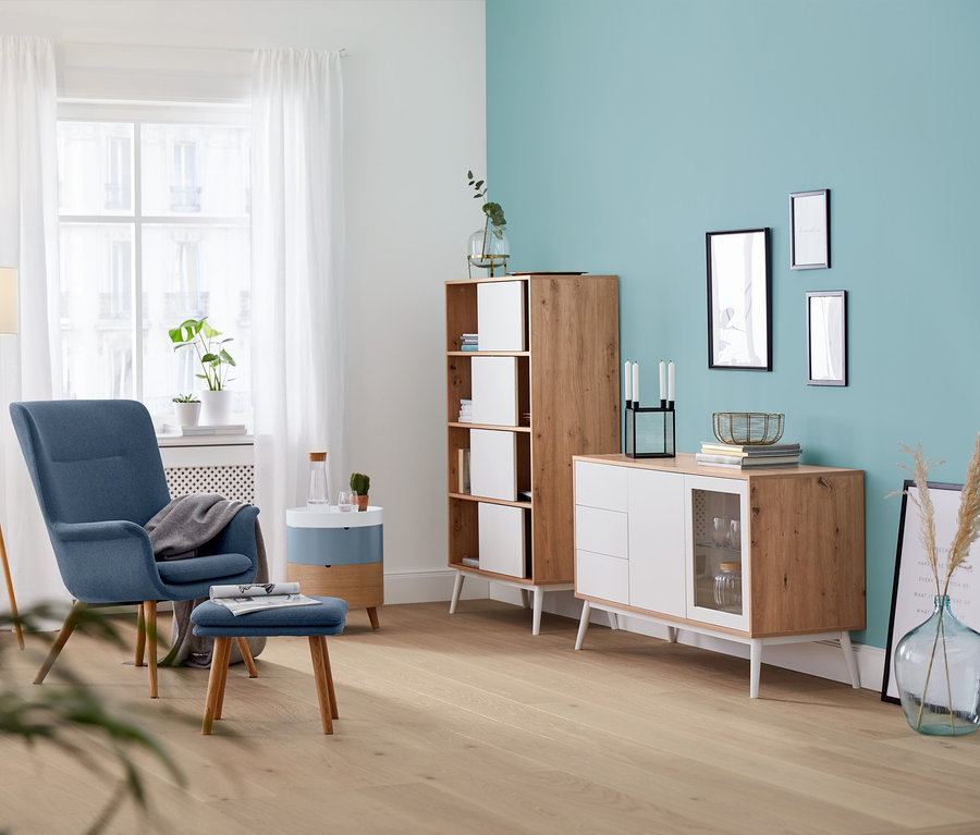 Wohnzimmer mit blauem Sessel, Hocker und hölzerner Stehleuchte »Dreibein«.