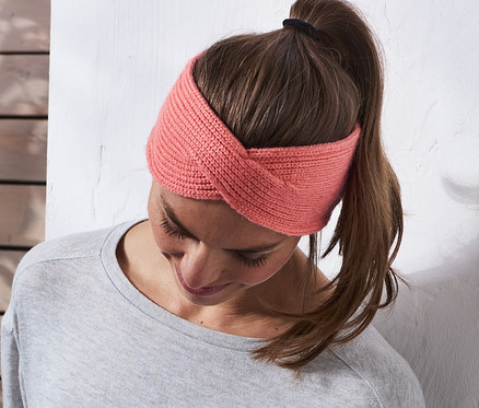 Frau mit Strick-Stirnband lehnt an einer Wand.