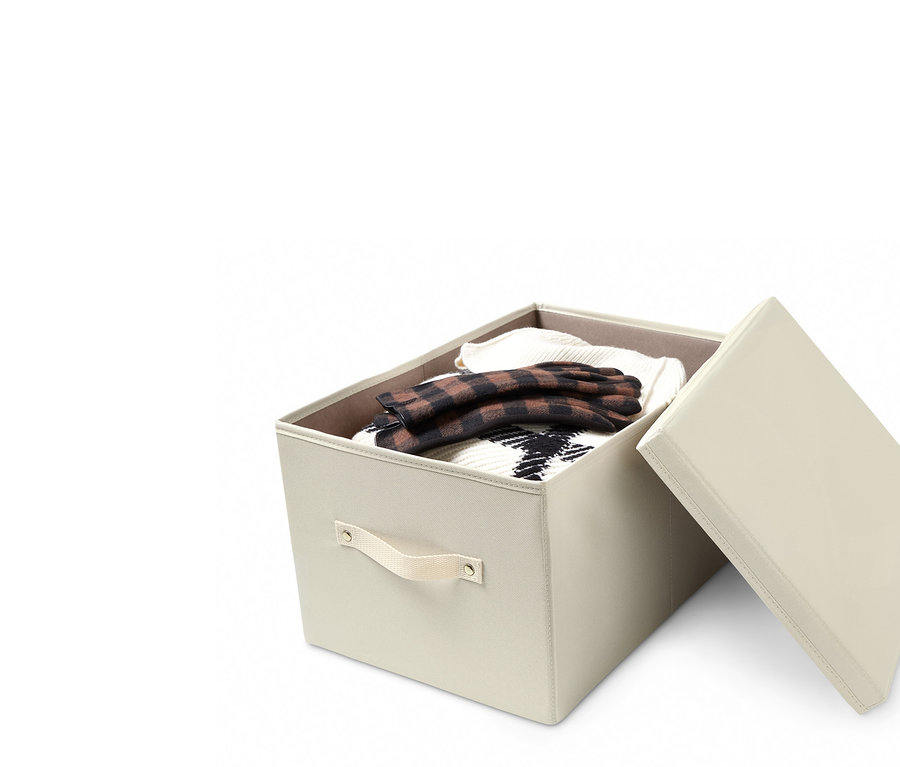 Geöffneter, cremefarbener Ordnungskiste mit Deckel, voll mit Kleidung, wobei der Deckel an die Seite der Kiste gelehnt ist.