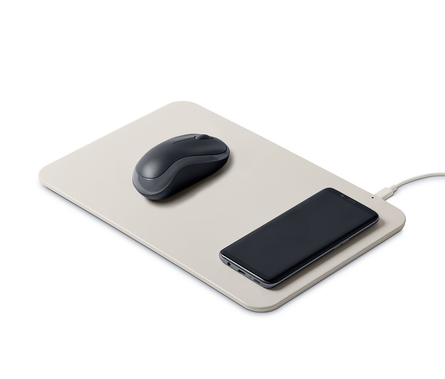 Eine Maus liegt auf einem Mauspad mit integriertem Ladegerät, auf dem ein Handy liegt.