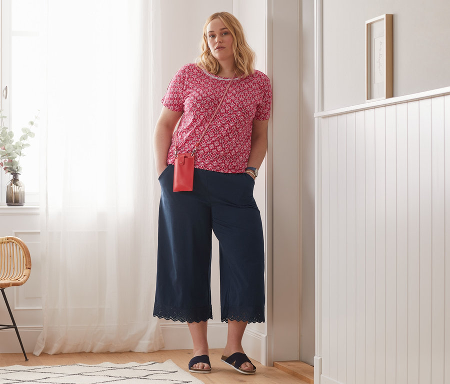Frau posiert in rot bedrucktem Blusenshirt und Culotte mit Stickerei.