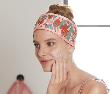 Frau trägt 2 Kosmetik-Stirnbänder und trägt Creme im Gesicht auf.