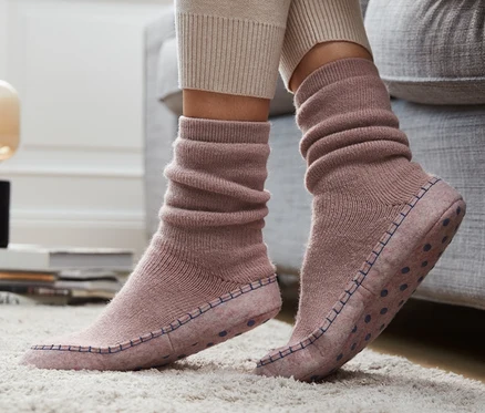 Beine in Hausschuh-Socken stehen auf einem Teppich neben einem Sofa.