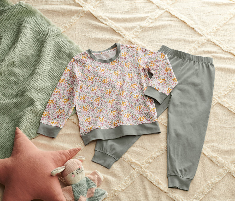 Auf einem Bett liegen ein Pyjama, eine grüne Decke, ein sternförmiges Kissen und ein Plüschtier.