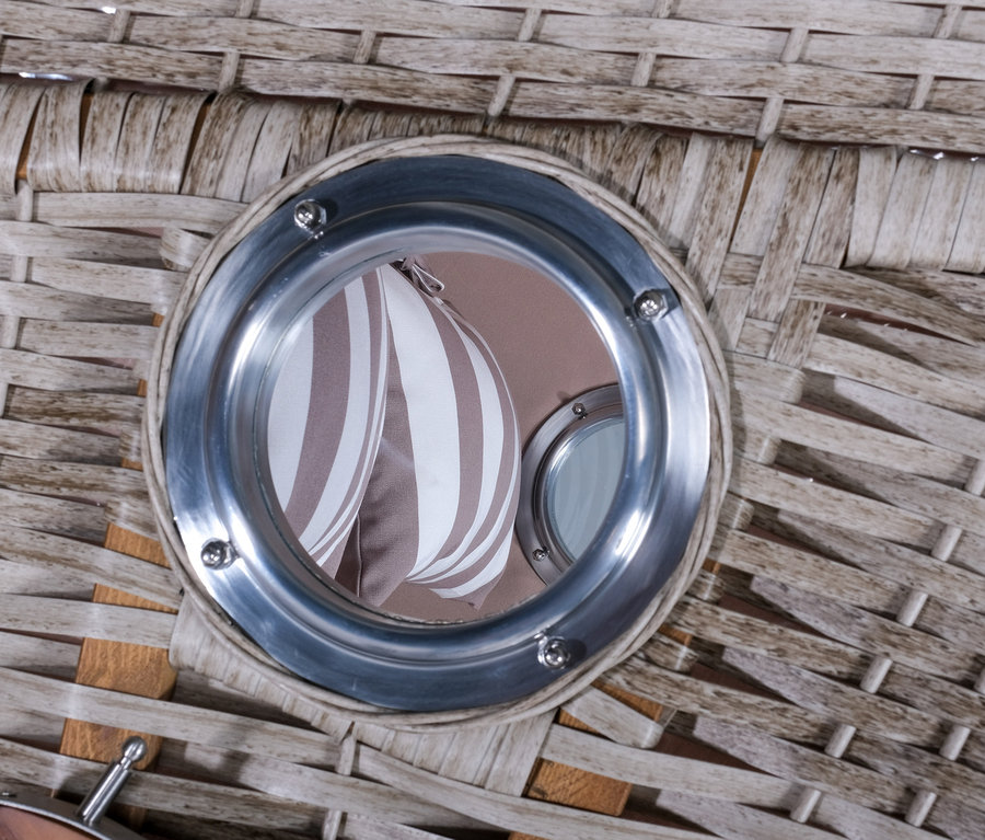 Detailansicht eines geflochtenen Strandkorbs mit rundem Fenster, durch das ein gestreifter Stoff sichtbar ist.