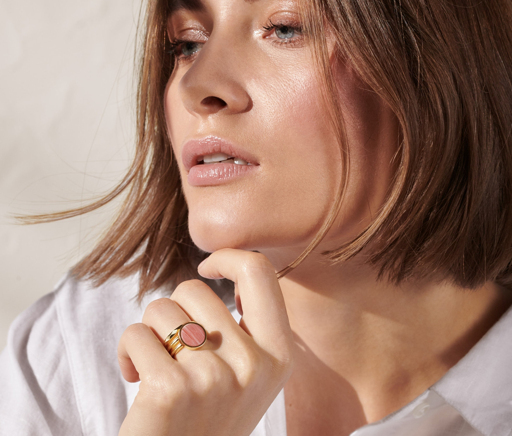 Frau mit hellbraunen Haaren berührt ihr Kinn mit der Hand, an der sie ein goldenes 3er-Ring-Set trägt.