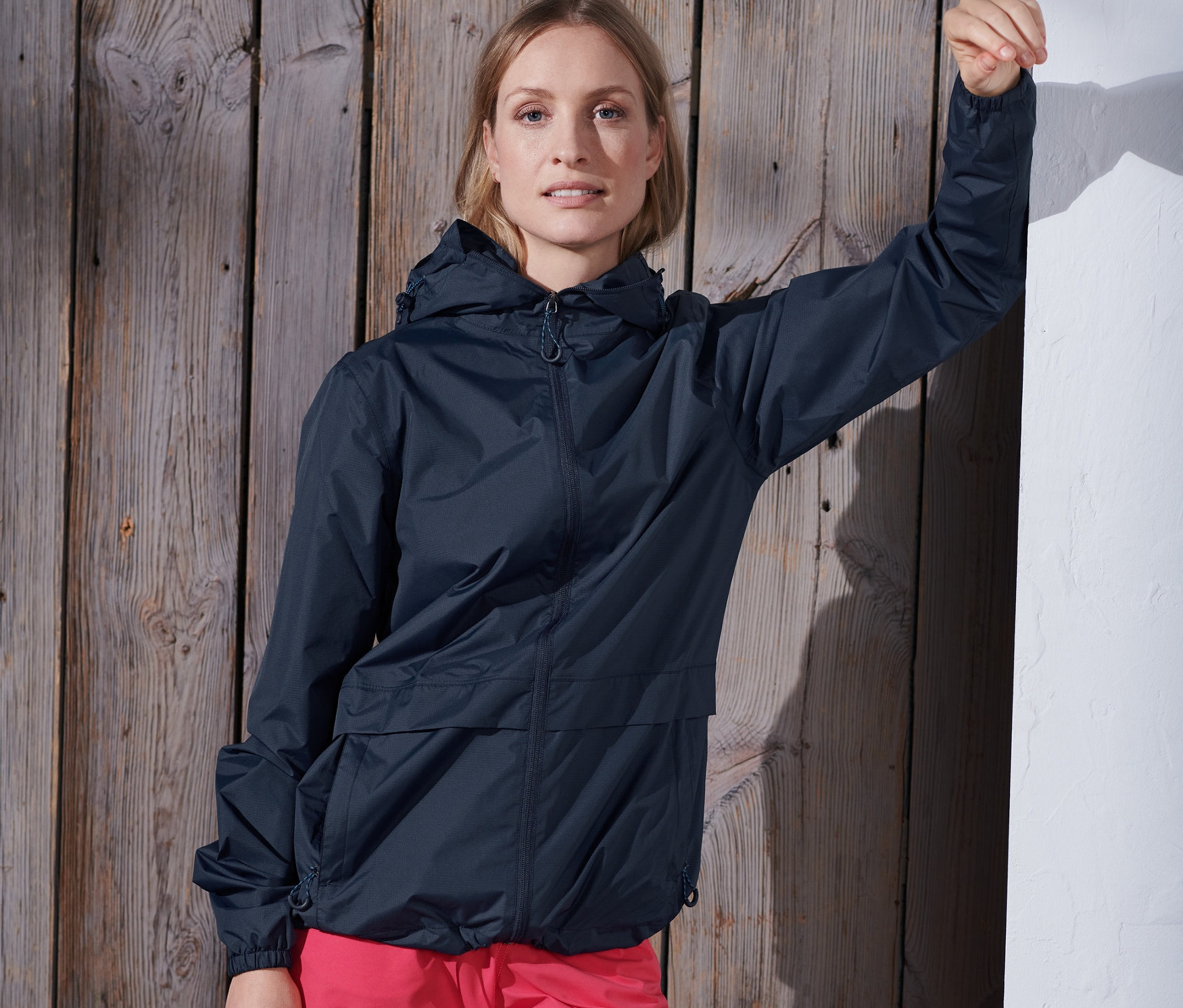 Frau an Wand angelehnt trägt dunkelblaue Lightweight-Regenjacke »pack me«.