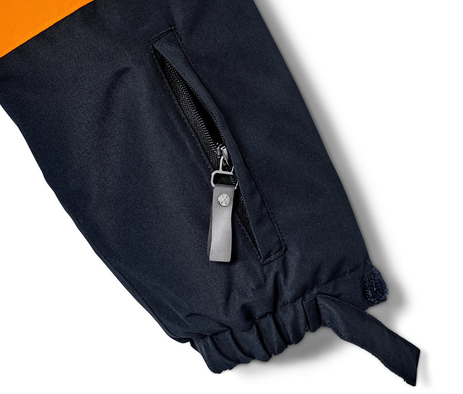 Detail einer Ski- und Snowboardjacke mit orangefarbenem Oberteil und dunkelblauem Unterteil, mit einer Reißverschlusstasche.