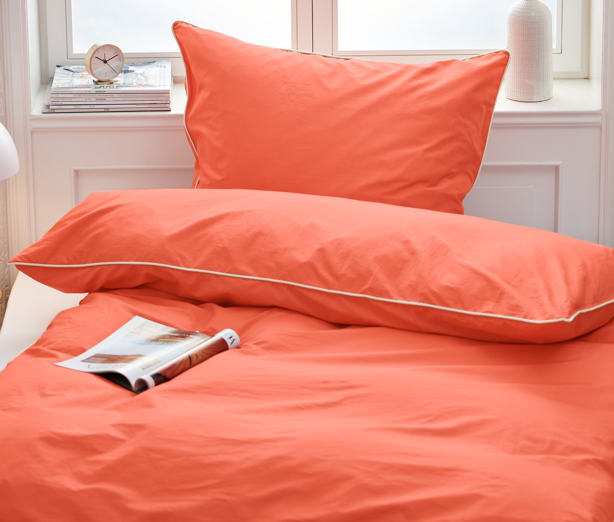 Orangefarbene Premium-Baumwoll-Bettwäsche in Normalgröße auf einem Bett mit einer Zeitschrift.