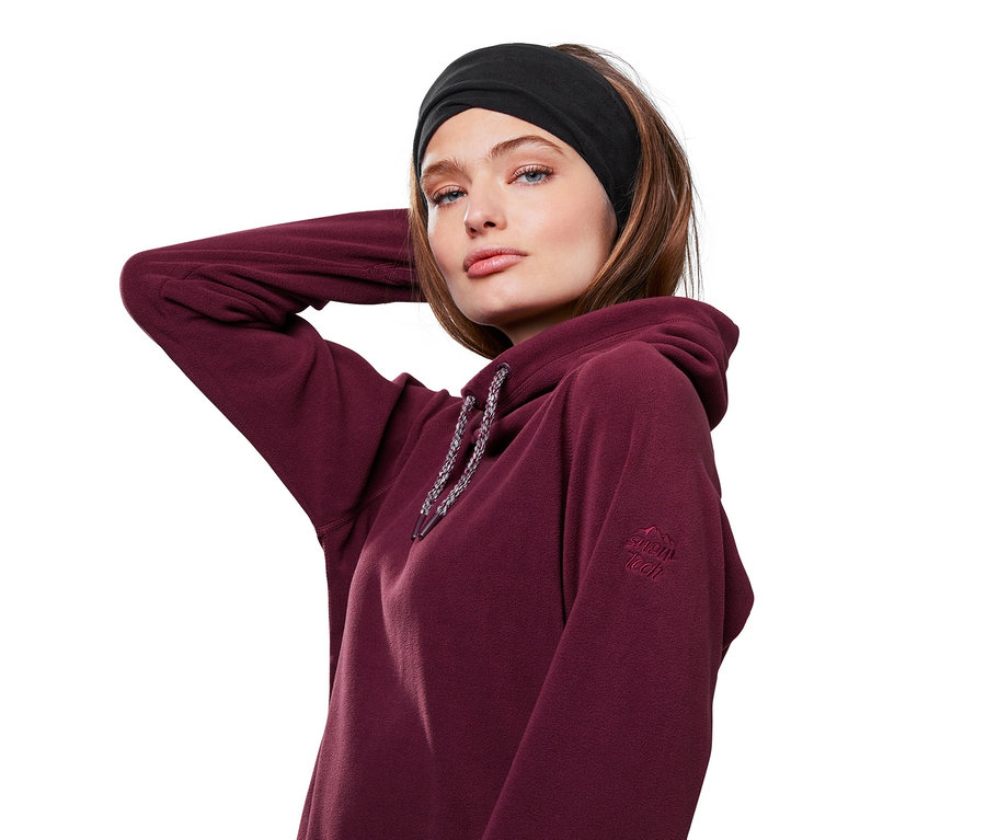 Frau posiert mit schwarzem Multifunktionsschal und Mütze auf dem Kopf und burgunderfarbenem Kapuzenpullover.