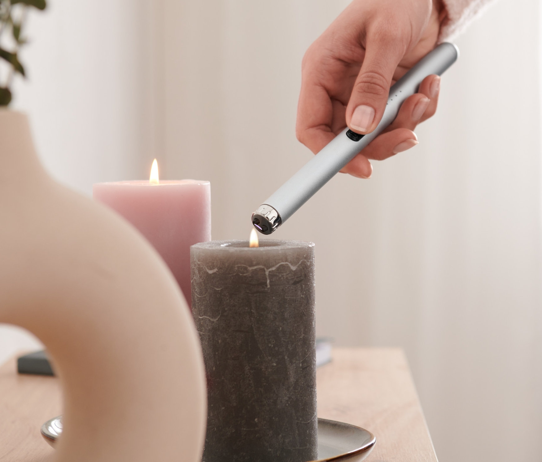 Frau zündet eine graue Kerze mit einem elektrischen Lichtbogen-Feuerzeug an.