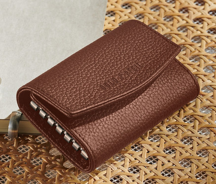 Ein braunes Leder-Schlüsseletui liegt auf einem Korbstuhl neben einem Stift und einem Notizblock. Im Bild ist ein »Goldpfeil« Leder-Schlüsseletui in Braun.