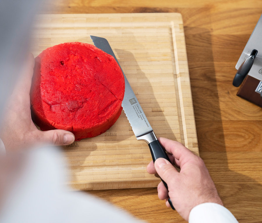Mann schneidet mit ZWILLING Brotmesser ein rotes Brot auf einem Holzbrett.