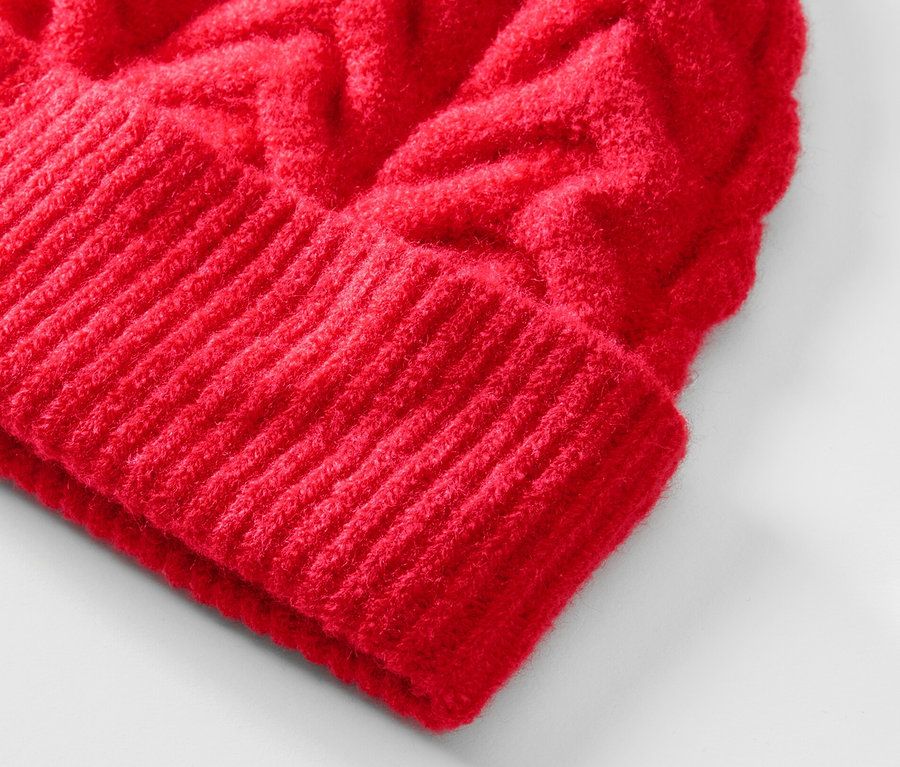 Detailaufnahme einer roten Strickmütze mit Zopfmuster.