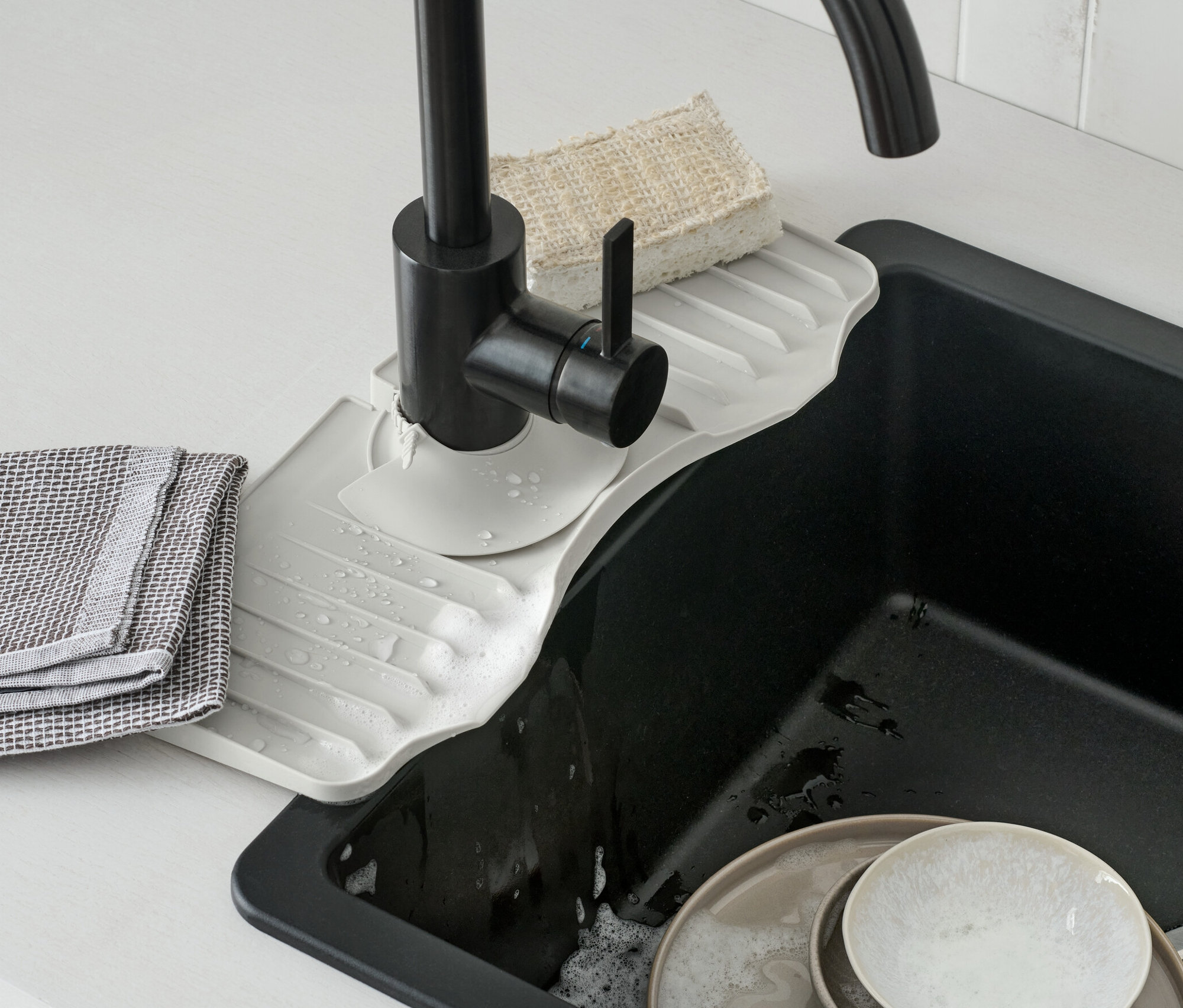 Eine Wasserhahn-Silikonablage befindet sich unter einem schwarzen Wasserhahn. Schmutziges Geschirr befindet sich im Spülbecken.