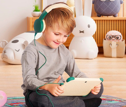 Ein Junge sitzt auf dem Boden und benutzt ein Tablet mit angeschlossenen Kopfhörern. Er trägt Fox & Sheep Kids Tablet »One« mit Kopfhörer.