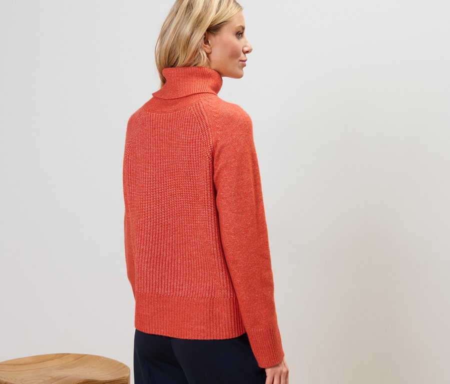 Rückansicht einer Frau in einem orangefarbenen Grobstrickpullover mit Rollkragen.