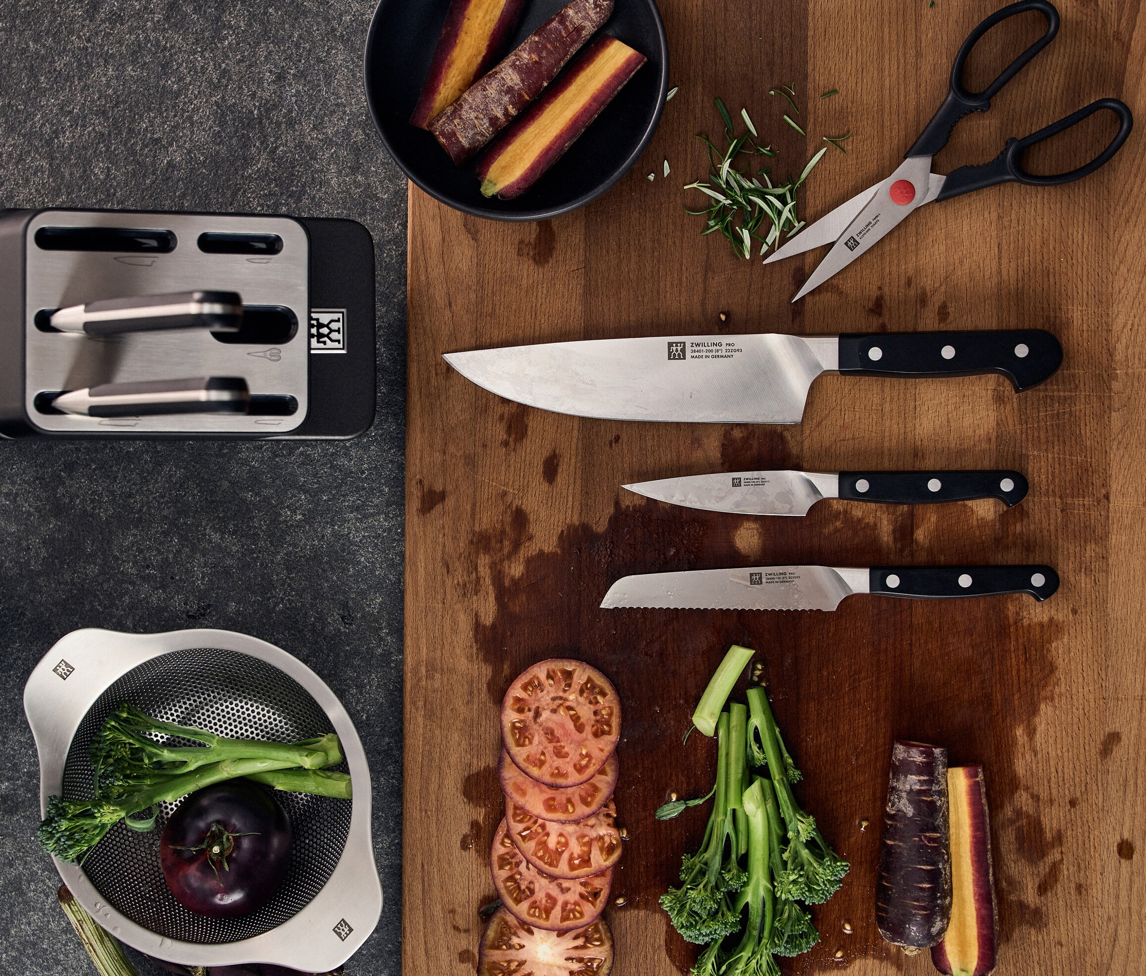 Auf einem Tisch liegen ein Messerblock, Messer, Schere, Gemüse und Kräuter.