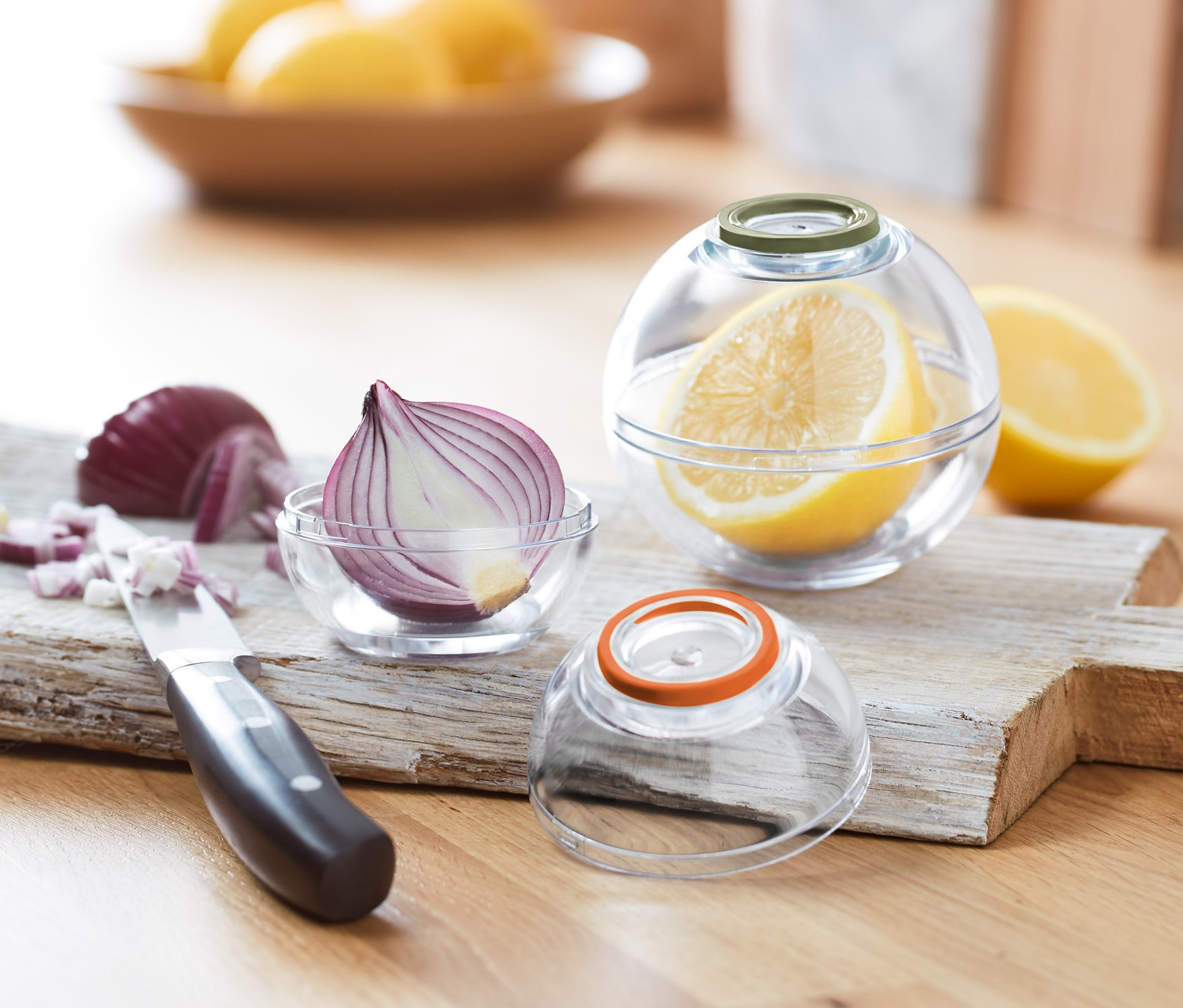 Halbe Zwiebel in einer 2 Frischhaltekugeln und halbe Zitrone in einer 2 Frischhaltekugeln auf einem Schneidebrett.