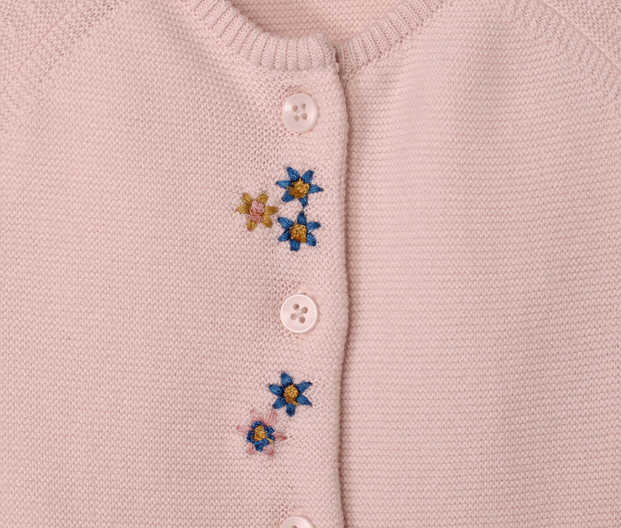 Detailansicht eines rosa Baby-Strickoveralls mit Knöpfen und Blumenstickereien.