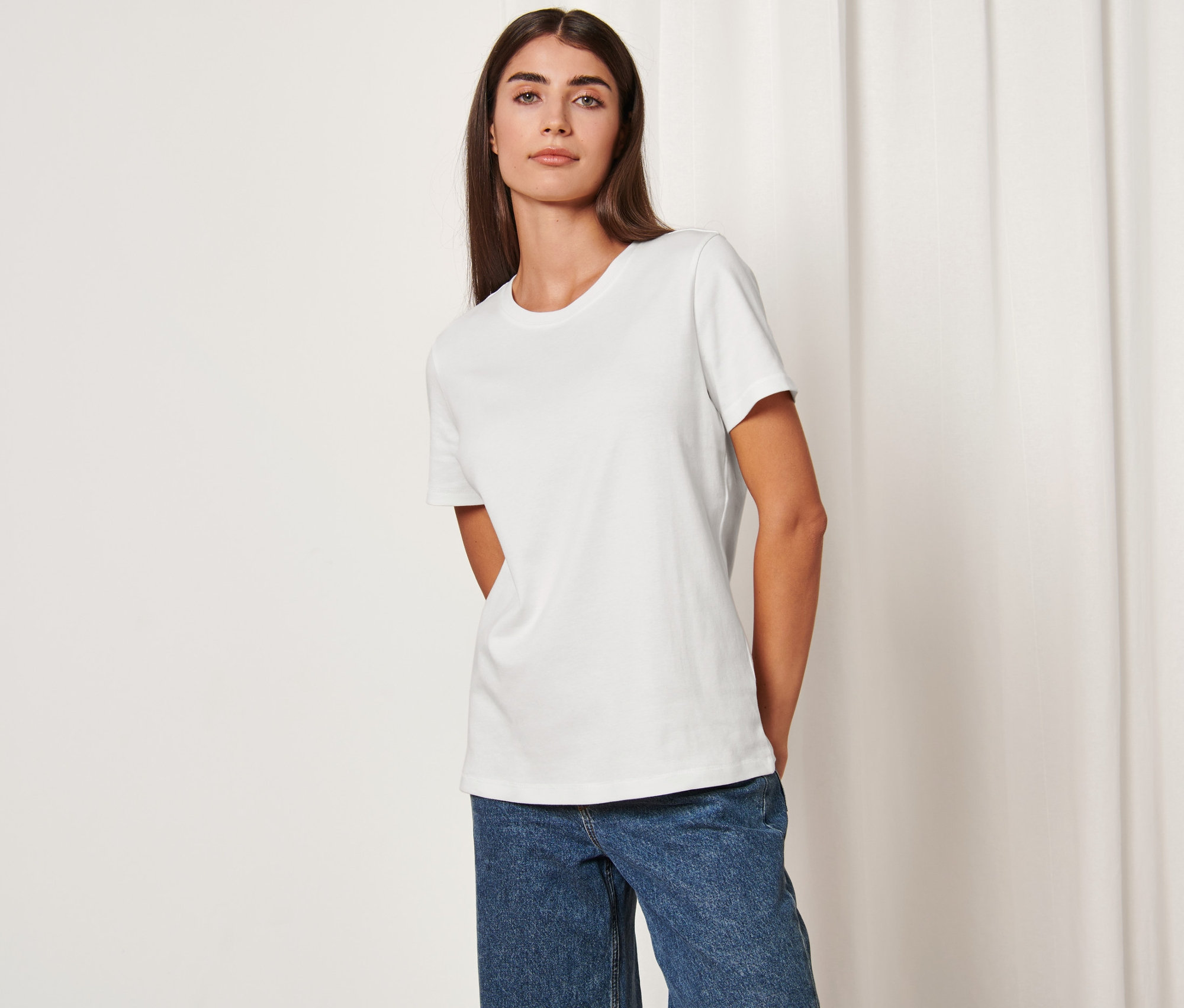 Frau trägt ein cremefarbenes Basic T-Shirt und Jeans.