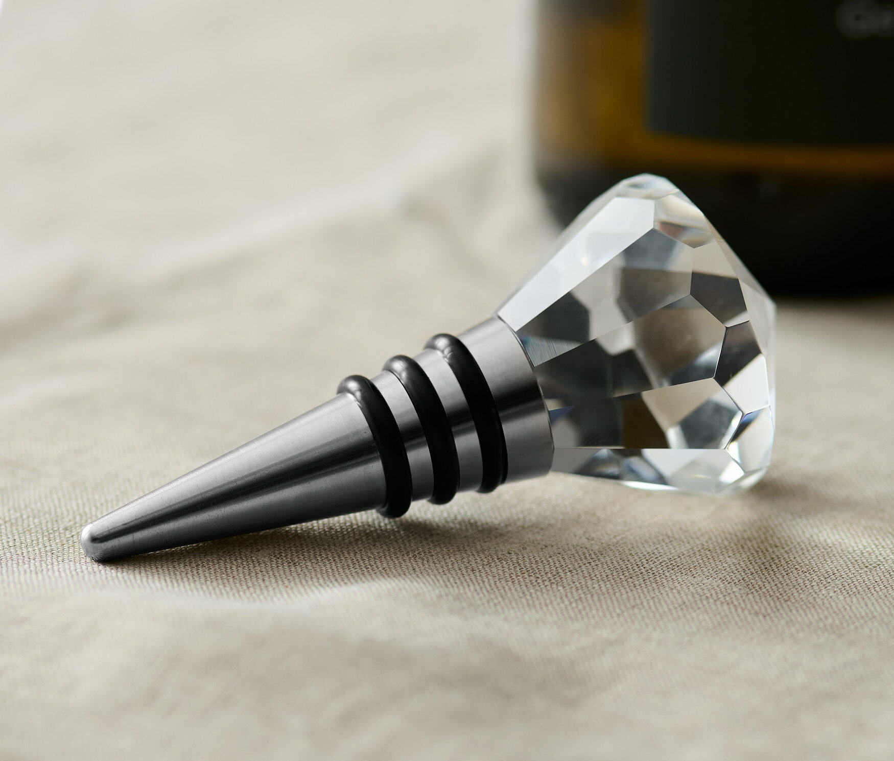 Ein Flaschenkorken mit Kristallverzierung liegt auf einem beigen Tuch.