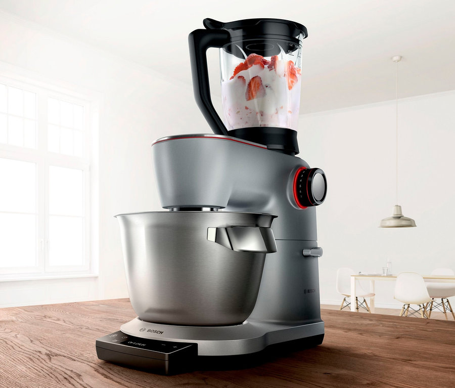 Silberne Bosch Küchenmaschine MUM9DT5S41 mit Edelstahlschüssel und Mixer mit Früchten auf einem Holztisch.
