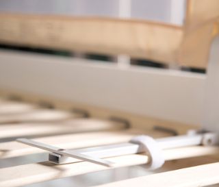 Detailansicht eines beigen roba Bettschutzgitters »Klipp-Klapp«, das an einem Bettrahmen befestigt ist.