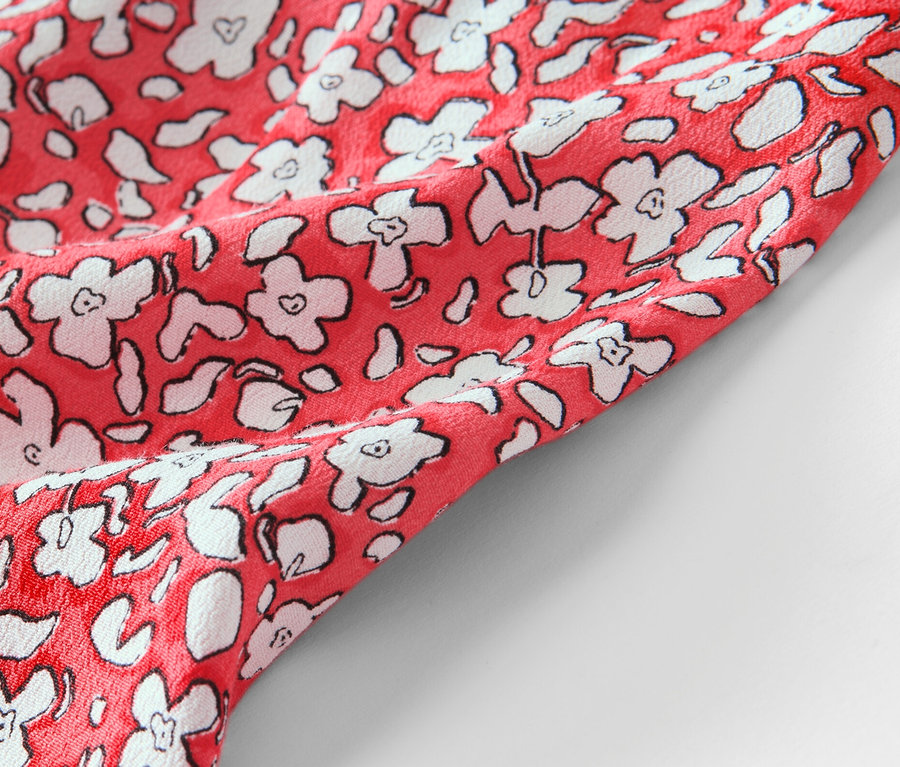 Detailansicht eines korallenfarbenen, bedruckten Midirocks.