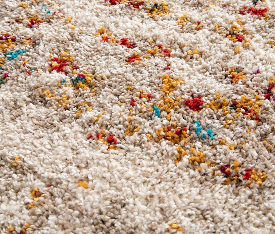 Nahaufnahme des beigen Hochflorteppichs »Himalaya« mit roten, gelben und türkisfarbenen Farbtupfern.