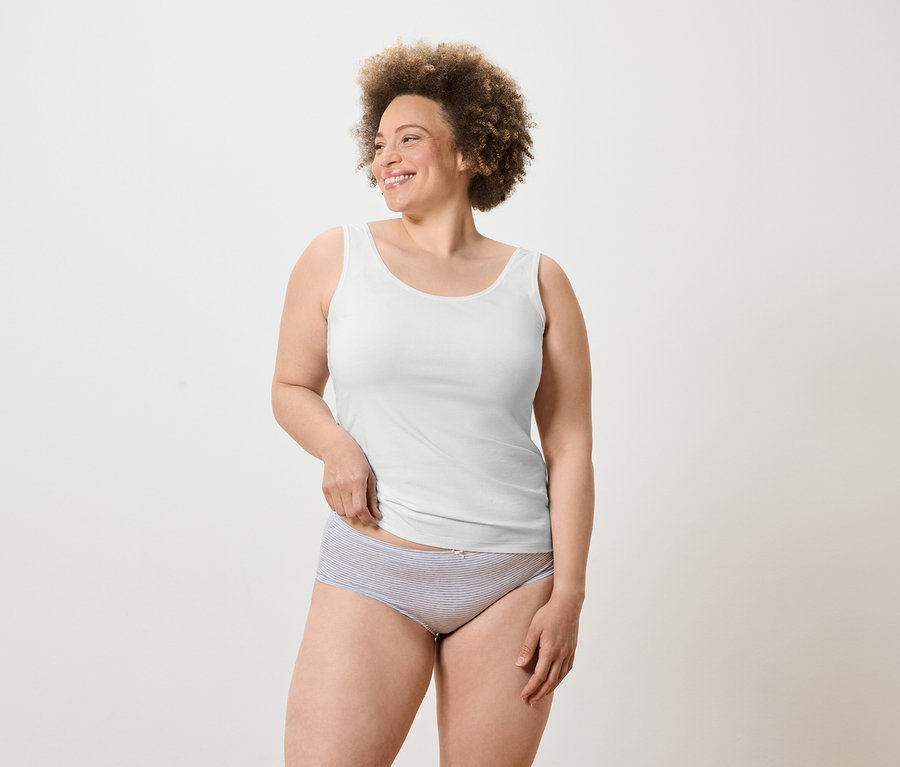 Eine lächelnde Frau mit Afro trägt ein weißes Tanktop und gestreifte Unterwäsche.