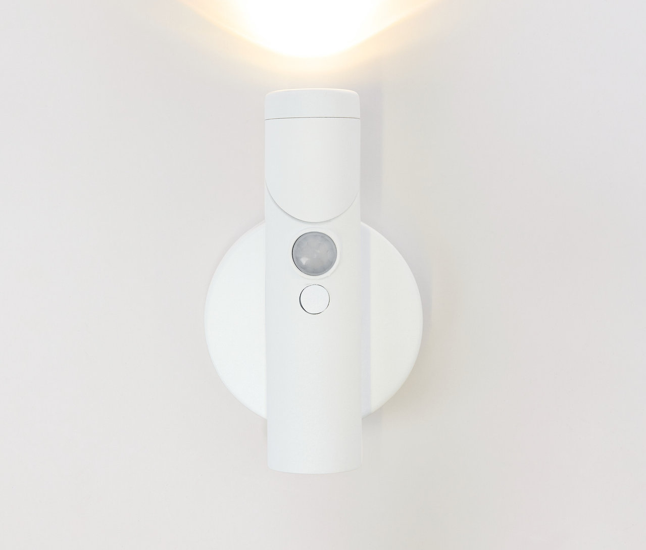 Weiße Wandleuchte mit Bewegungsmelder leuchtet an weißer Wand.