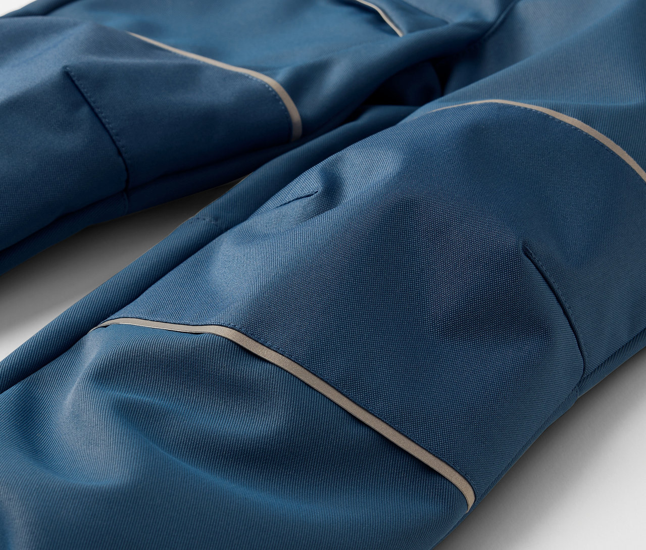 Detailaufnahme einer blauen Kinder-Softshellhose mit Taschen und Reflexdetails.