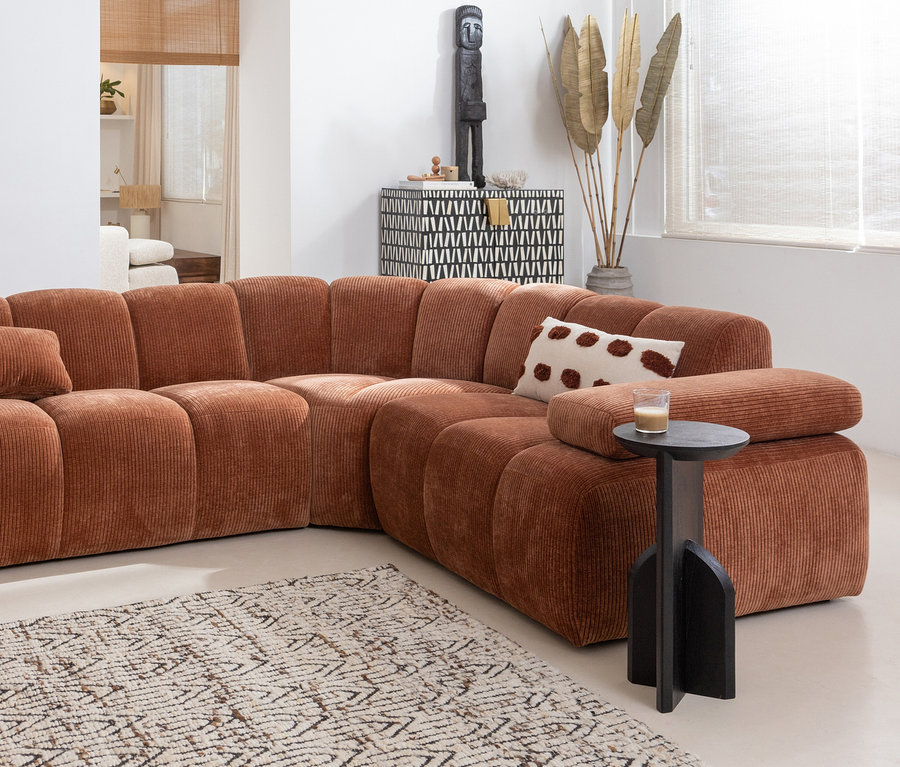 Detail eines Wohnzimmers mit braunem Ecksofa, Dekoschrank, schwarzem Beistelltisch und beigem Woood Joslin Teppich.