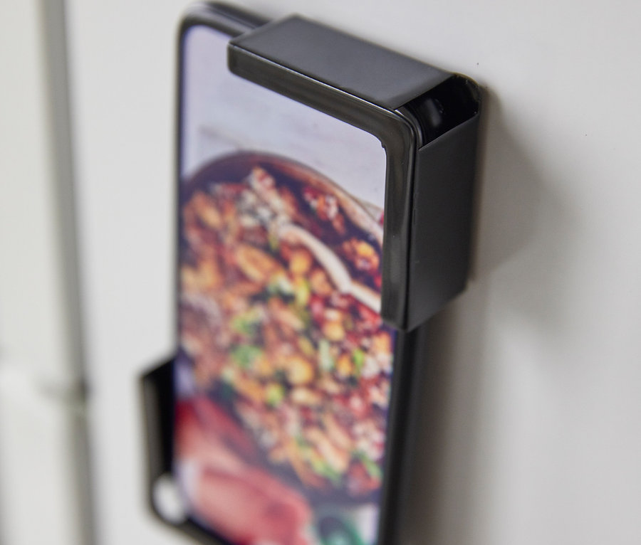Ein an einer weißen Wand befestigtes Handy mit einem schwarzen Yamazaki Tablethalter »TOWER«.