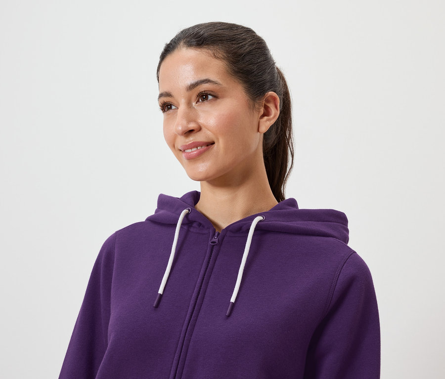 Frau mit braunen Haaren im Pferdeschwanz trägt einen violetten Kapuzenpullover mit Reißverschluss.