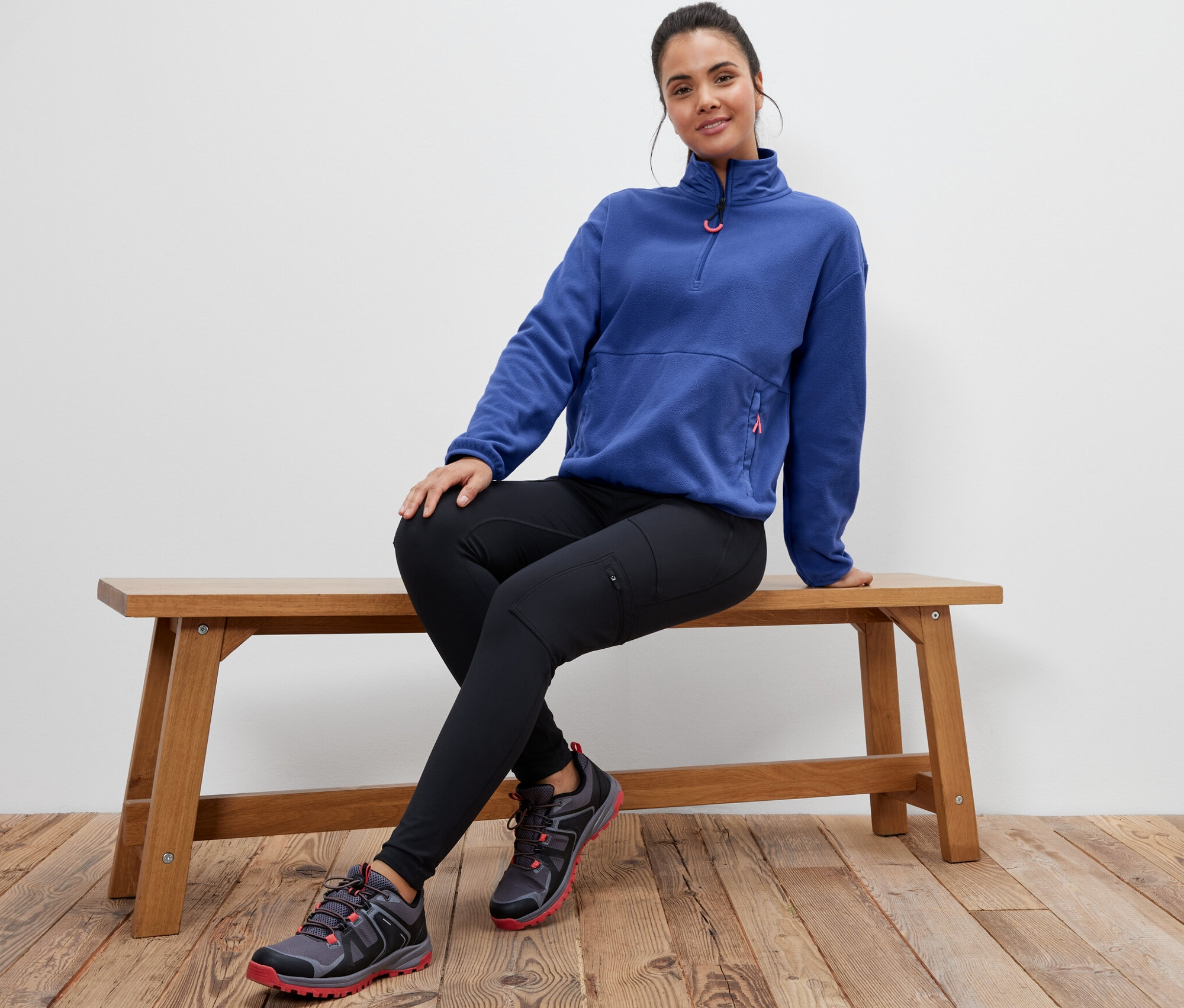 Eine Frau sitzt auf einer Bank und trägt einen blauen Fleecepullover.