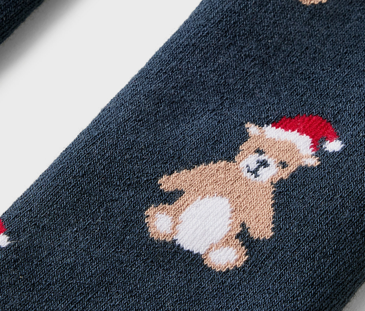 Detailaufnahme einer blauen Socke mit Teddybären mit roten Weihnachtsmützen.